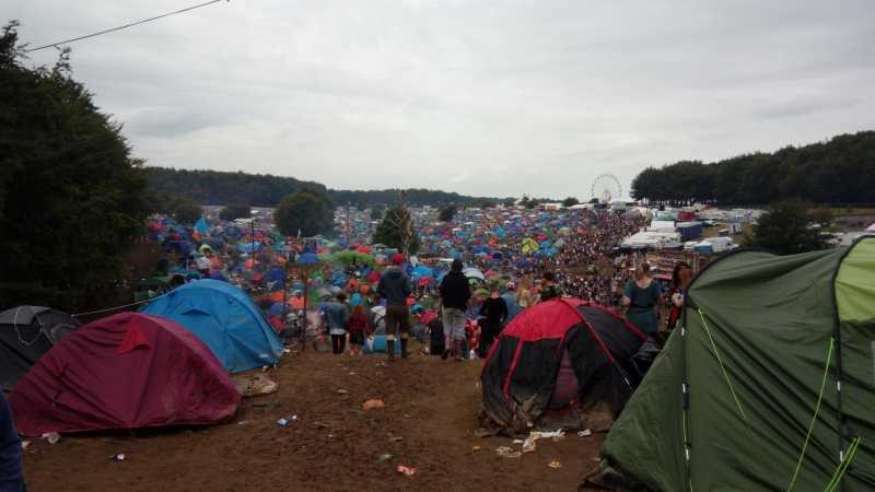 Foto dunha enorme acampada xunto a un festival de música que se ve ao fondo. Hai varios miles de tendas de campaña e moitísima xente e abundantes desperdicios polo chan. 