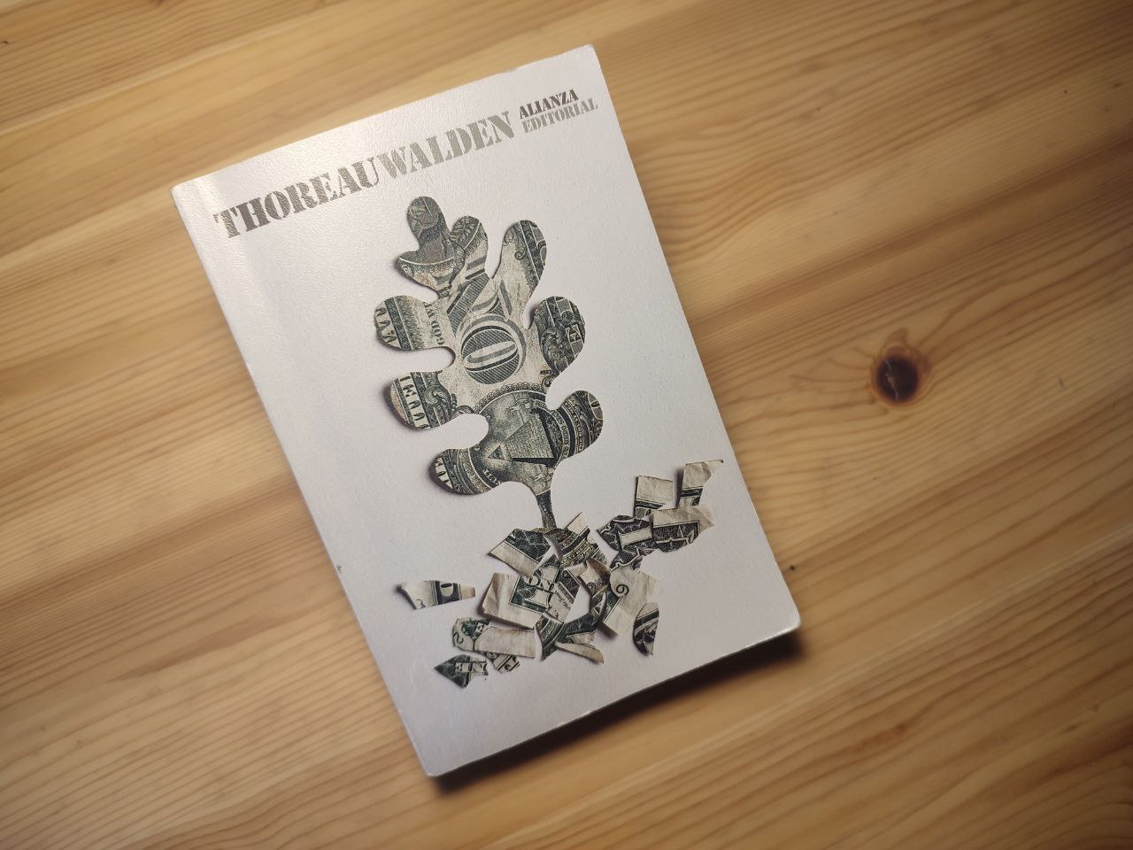 Libro do escritor Thoreau con título Walden, da editorial Alianza sobre a madeira clara dunha mesa. Na portada vese a forma dunha folla de carballo feita dunh billete de dólar.